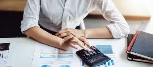 Woman sitting at desk with calculator and papers, working on finances.