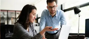 A man and woman collaborating on a laptop in a modern office setting.