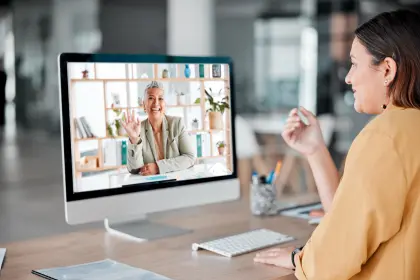 Woman sitting at desk with computer screen displaying video call.