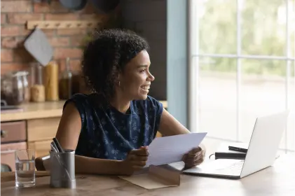 Woman sitting at table with laptop and paper, working diligently.