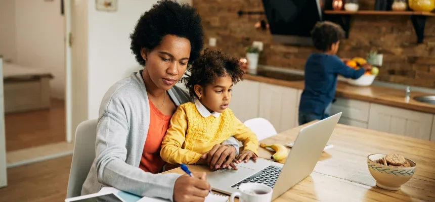 A woman and child sitting at a table with a laptop.