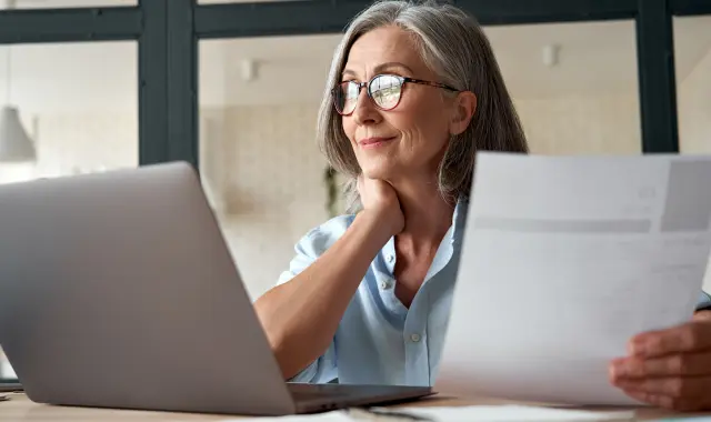 Professional woman wearing glasses working on laptop at desk.