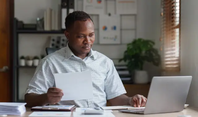 A man sitting at a desk with a laptop and paper.