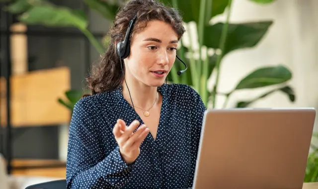 A woman with a headset sitting at a desk with a laptop.