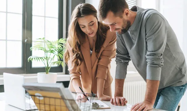 A man and woman standing at a desk, focused on a laptop screen.