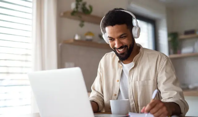 A man smiling while wearing headphones and using a laptop.