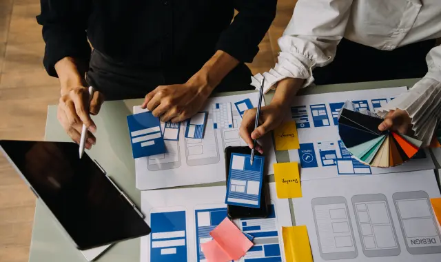 A pair of people brainstorming and creating a design together, using a laptop and drawing tools.