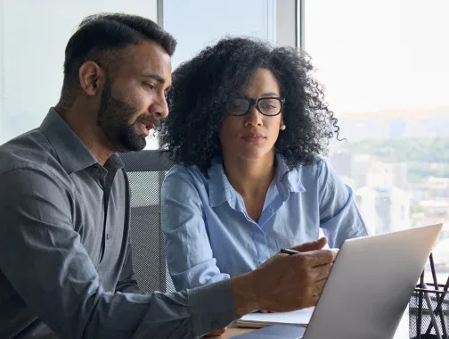 Two professionals discussing work on a laptop in an office setting.