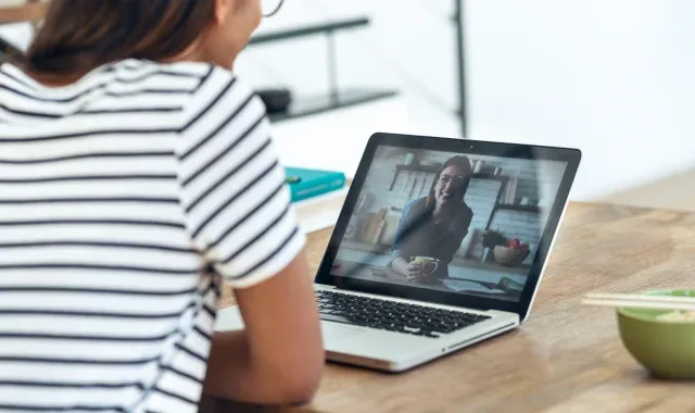 Woman sitting at table with laptop and bowl of food.