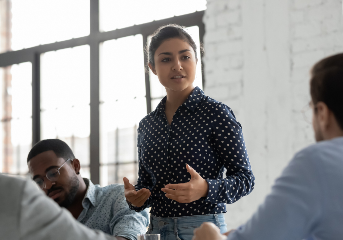 A woman presents confidently to an engaged audience, sharing insights and information in a professional setting.