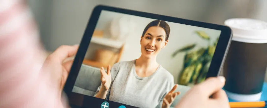 Woman holding tablet with video chat displayed.