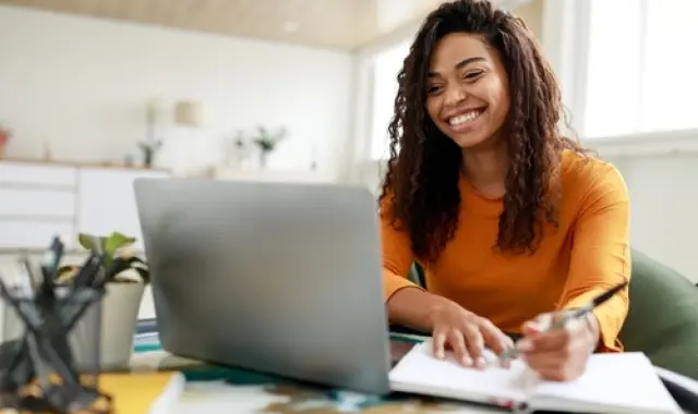 A woman smiling at her desk with a laptop.