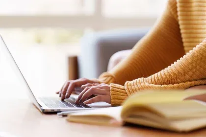 A woman in a yellow sweater typing on her laptop.