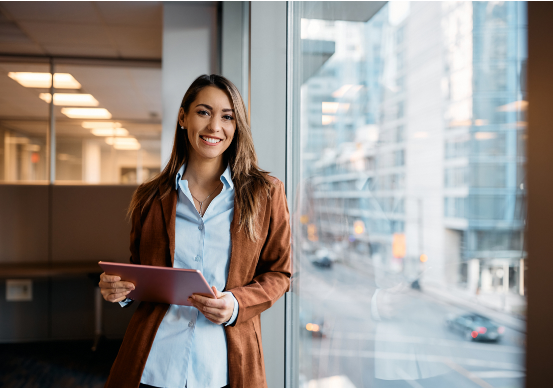 A professional woman in a business suit confidently holds a tablet, showcasing her readiness for work and technology.