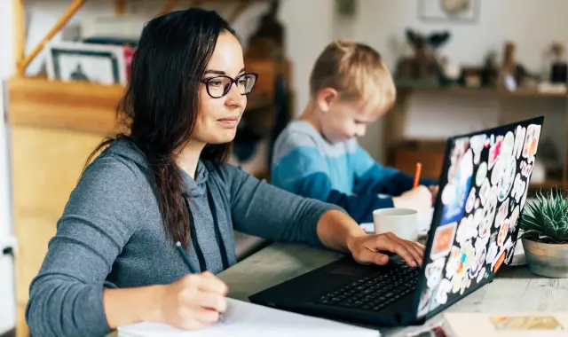 Woman with glasses and child sitting at table with laptop, working together on a project.