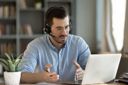 A man wearing a headset and sitting at a desk with a laptop.